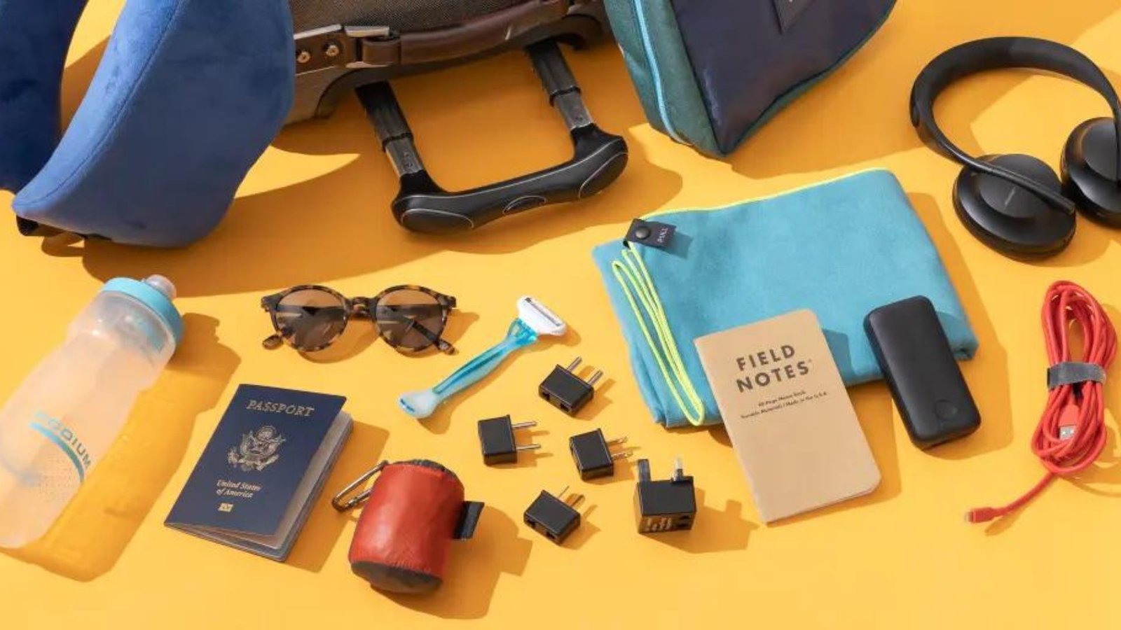 a passport, headphones, juice bottle, charger, monarch bag, etc showing travel gear and gadgets 