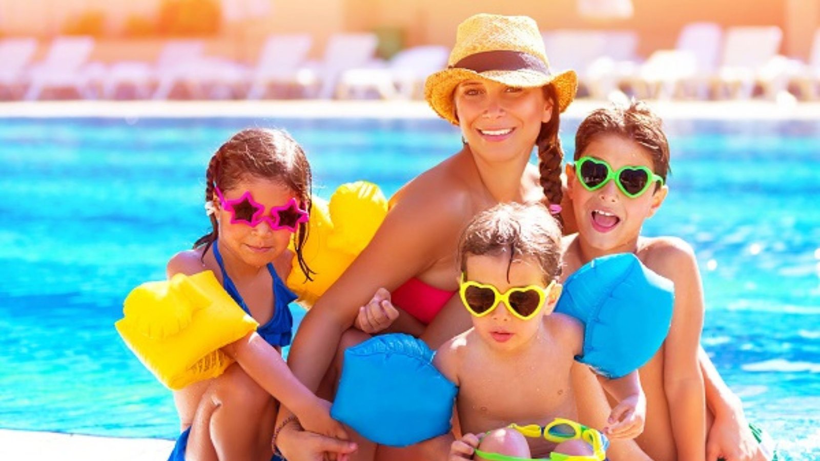 three children wearing shades and a mother wearing a sun hat on a holiday showing family-friendly travel, and a background of water