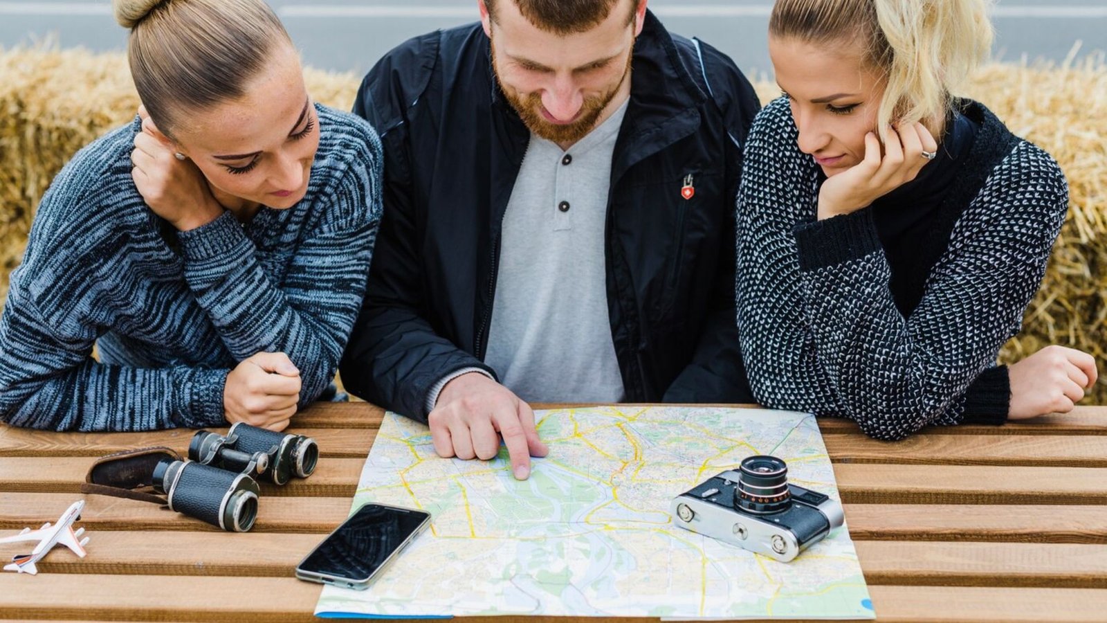 three people reading a map, a camear and a phone on the tabble showing travelling challenge strategies 